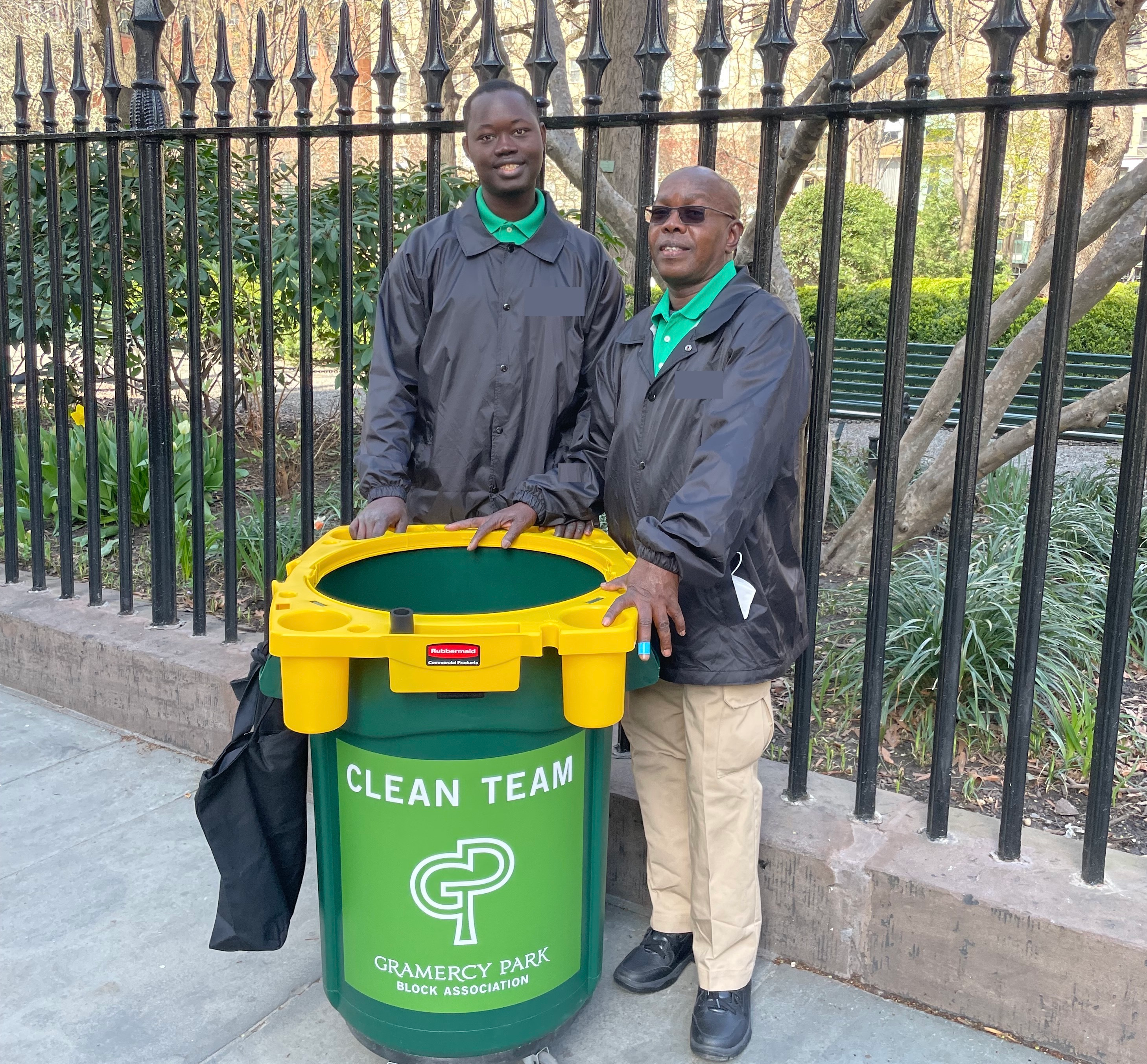 Mamadou Tall and Saliou Diop stand beside the green and yellow the Block Association’s Clean Team cart at the park fence.