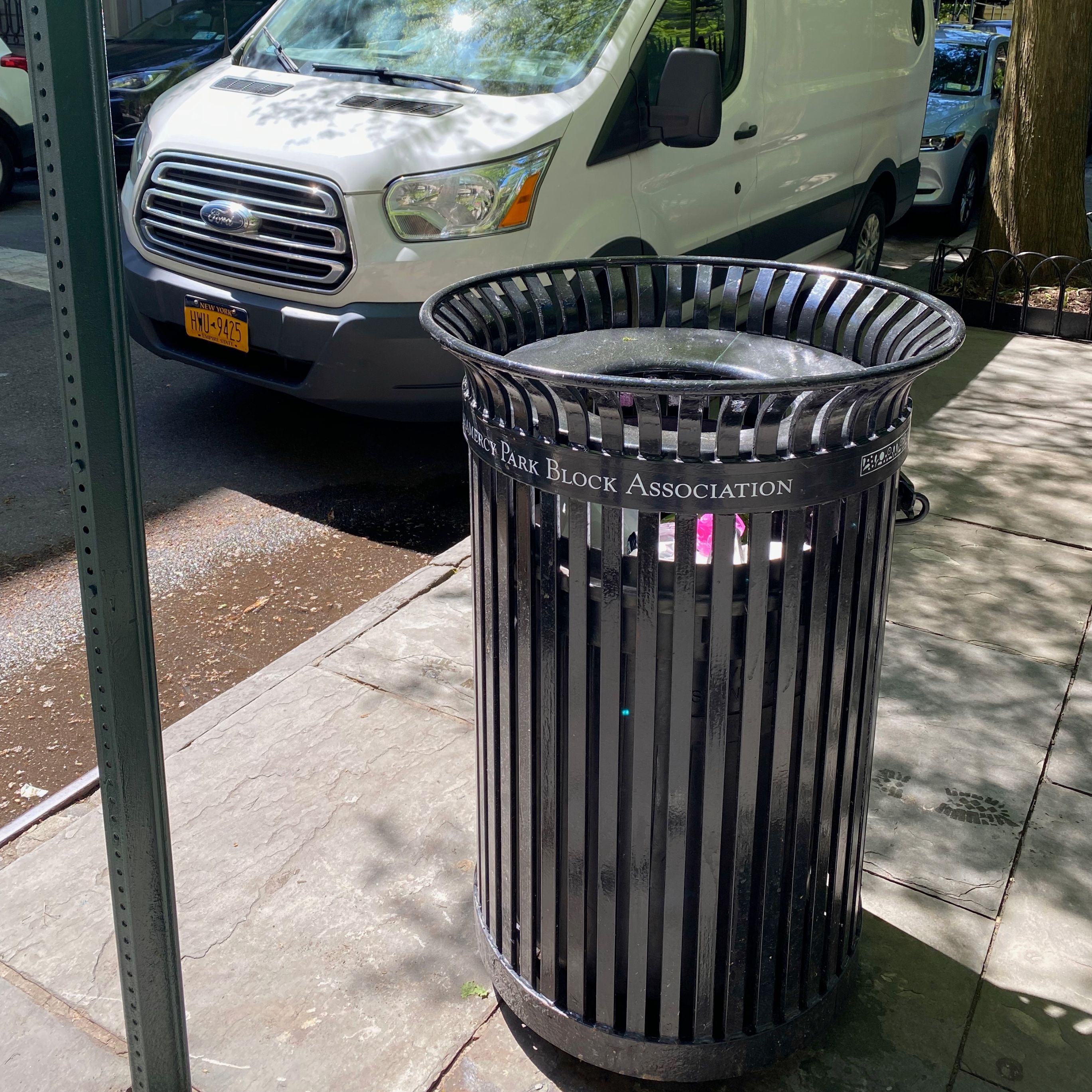 The matching sidewalk trash receptacle is cleared, with the sidewalk around it free of loose rubbish.