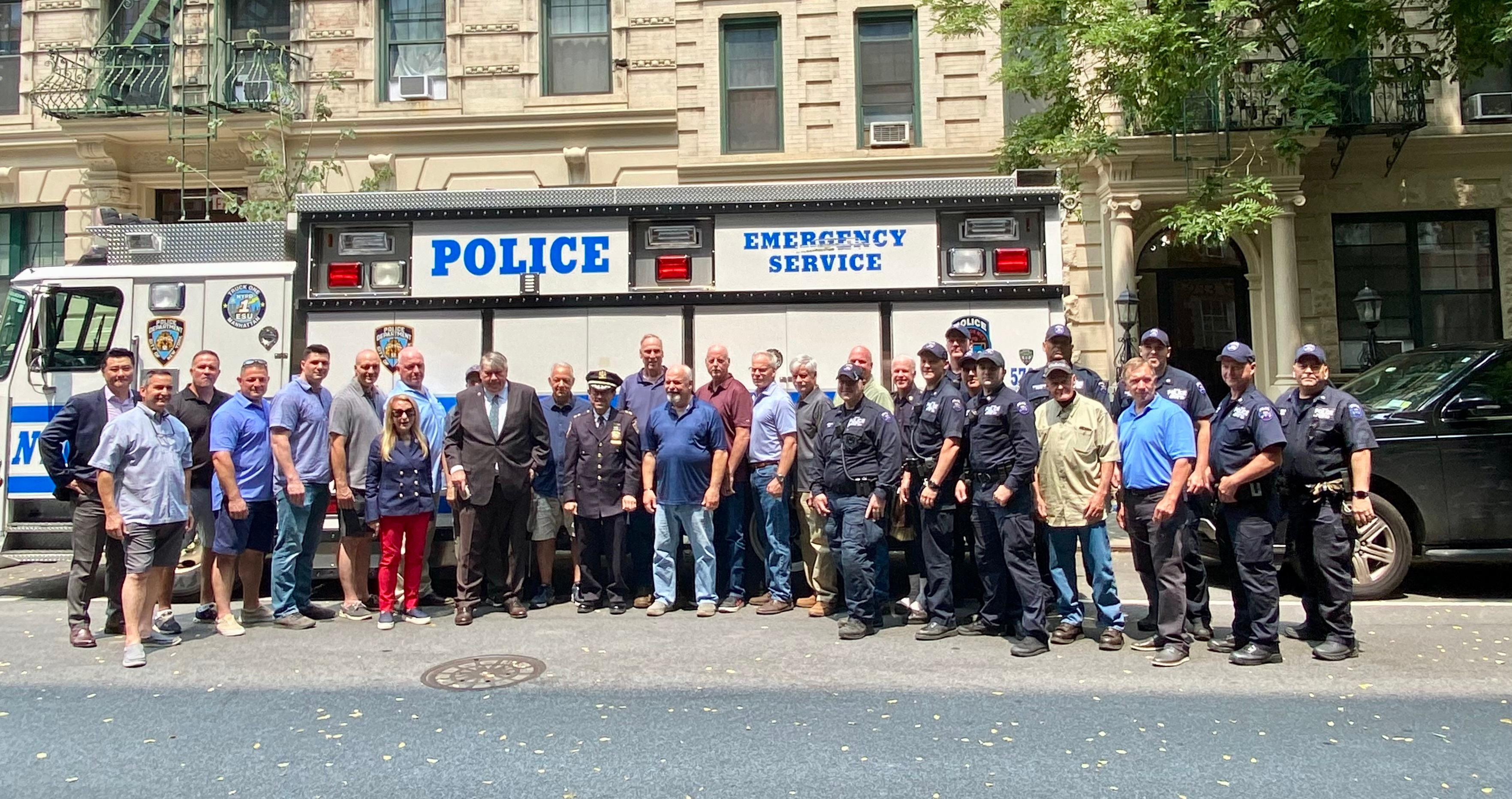 A group gathers on the street in front of an NYPD Emergency Service vehicle for the retirement event honoring Assistant Chief Gin Yee.