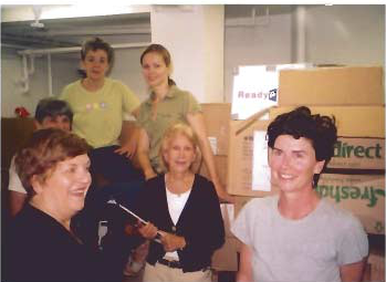 Volunteers stand among boxes of clothing and household supplies in a collection room.