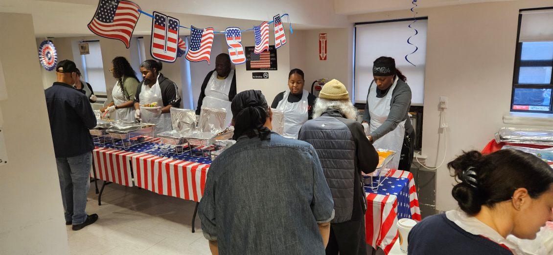 Guests and volunteers gather beside a buffet table decorated in red, white and blue at Kenmore Hall.