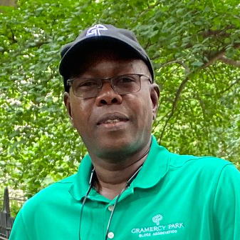 Portrait of Mamadou Tall wearing a green polo shirt, glasses and a dark cap outdoors.