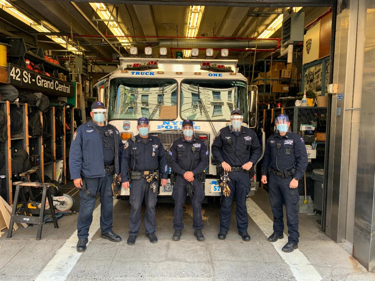 Five masked people stand in a garage in front of an NYPD Emergency Service truck.