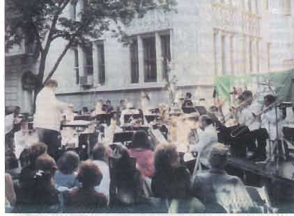 An orchestra performs on Gramercy Park East with an audience gathered in front.