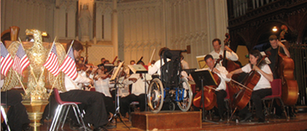 A young guest conductor faces the orchestra from a wheelchair in the church.