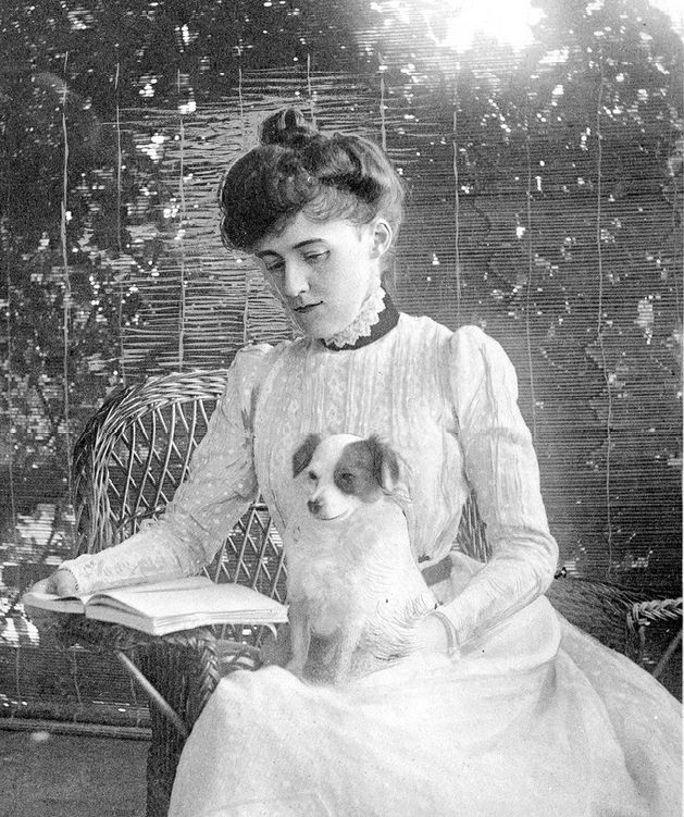 Edith Wharton seated reading beside a small dog.