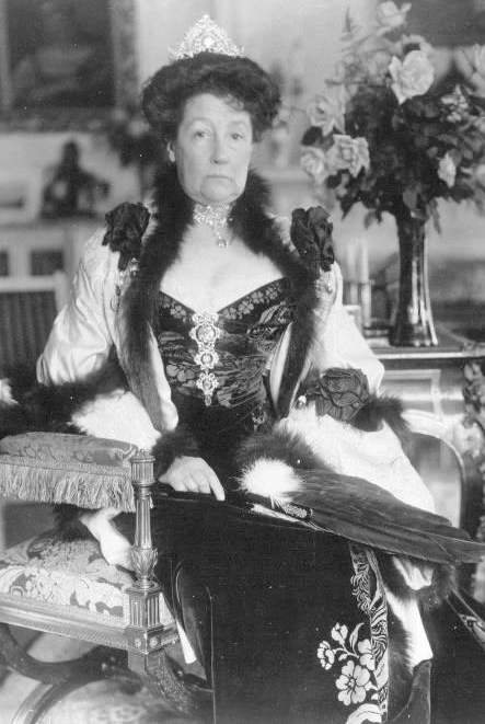 Mamie Fish seated in a formal gown with a long fan.
