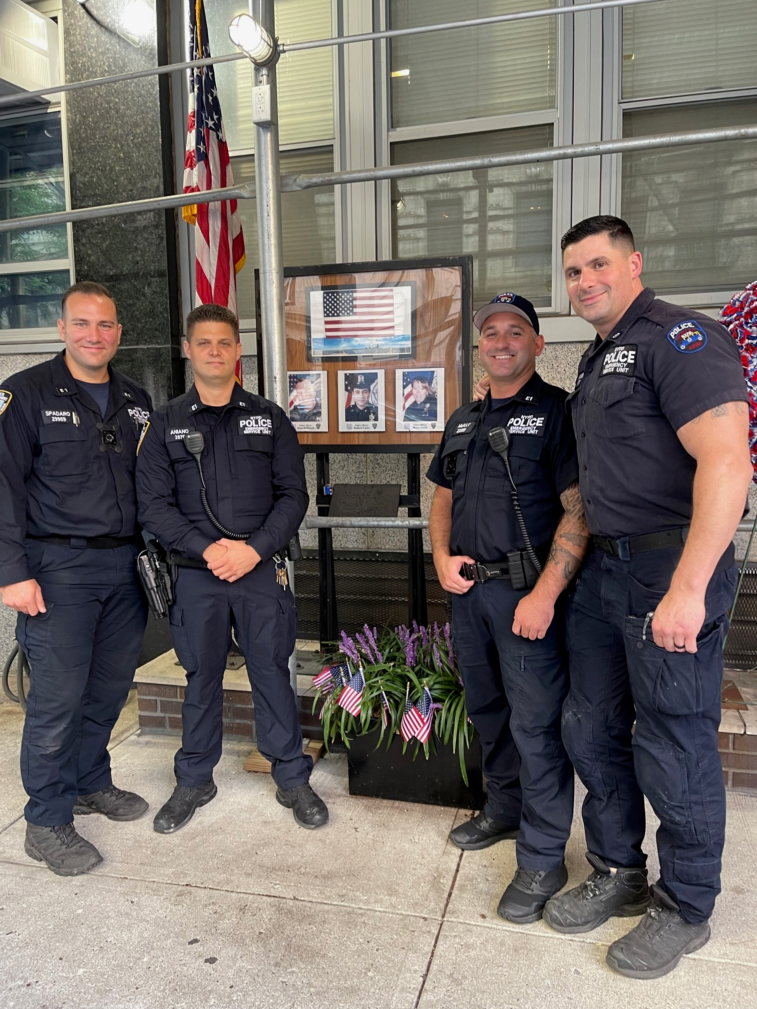 Four officers stand beside flowers and a memorial display at the 13th Precinct Remembrance Garden.