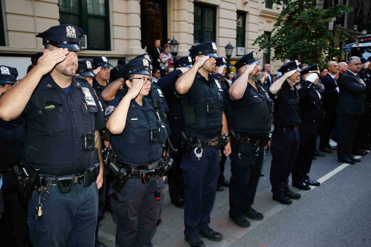 Uniformed officers stand in rows and salute outside the 13th Precinct.