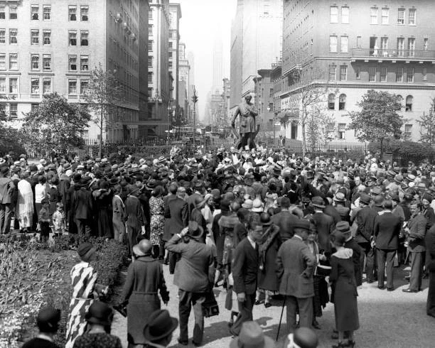 A crowd gathers around the Edwin Booth statue, looking north toward Lexington Avenue.
