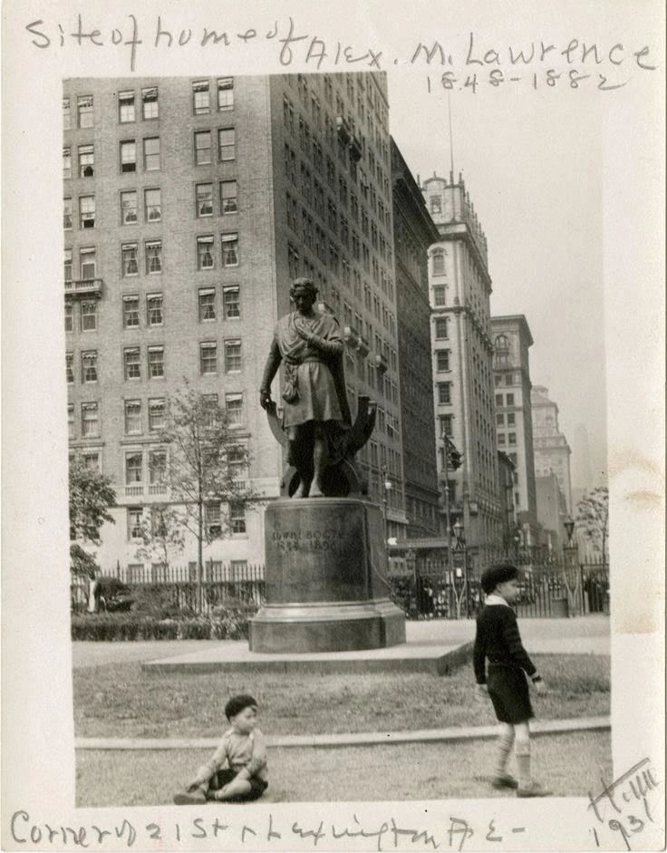 Two children beside the Edwin Booth statue, with Gramercy Park’s north-side buildings behind them; the mounted photograph retains its handwritten archival notes.