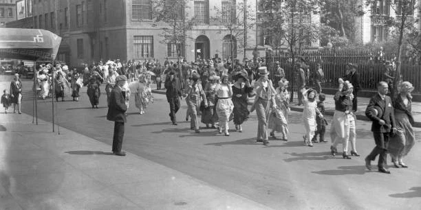 Adults and children in historic dress parade beside the Park.