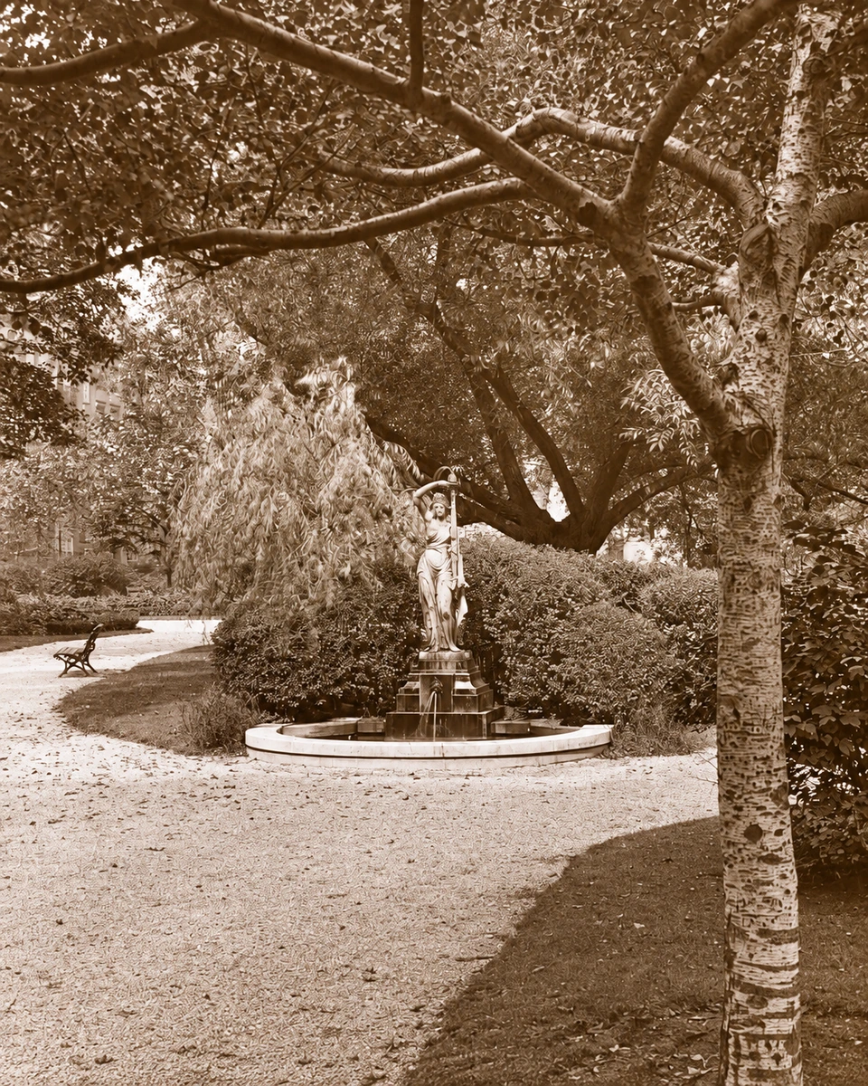 A historic lantern-slide view of the eastern nymph fountain framed by low shrubs and flowering plants.