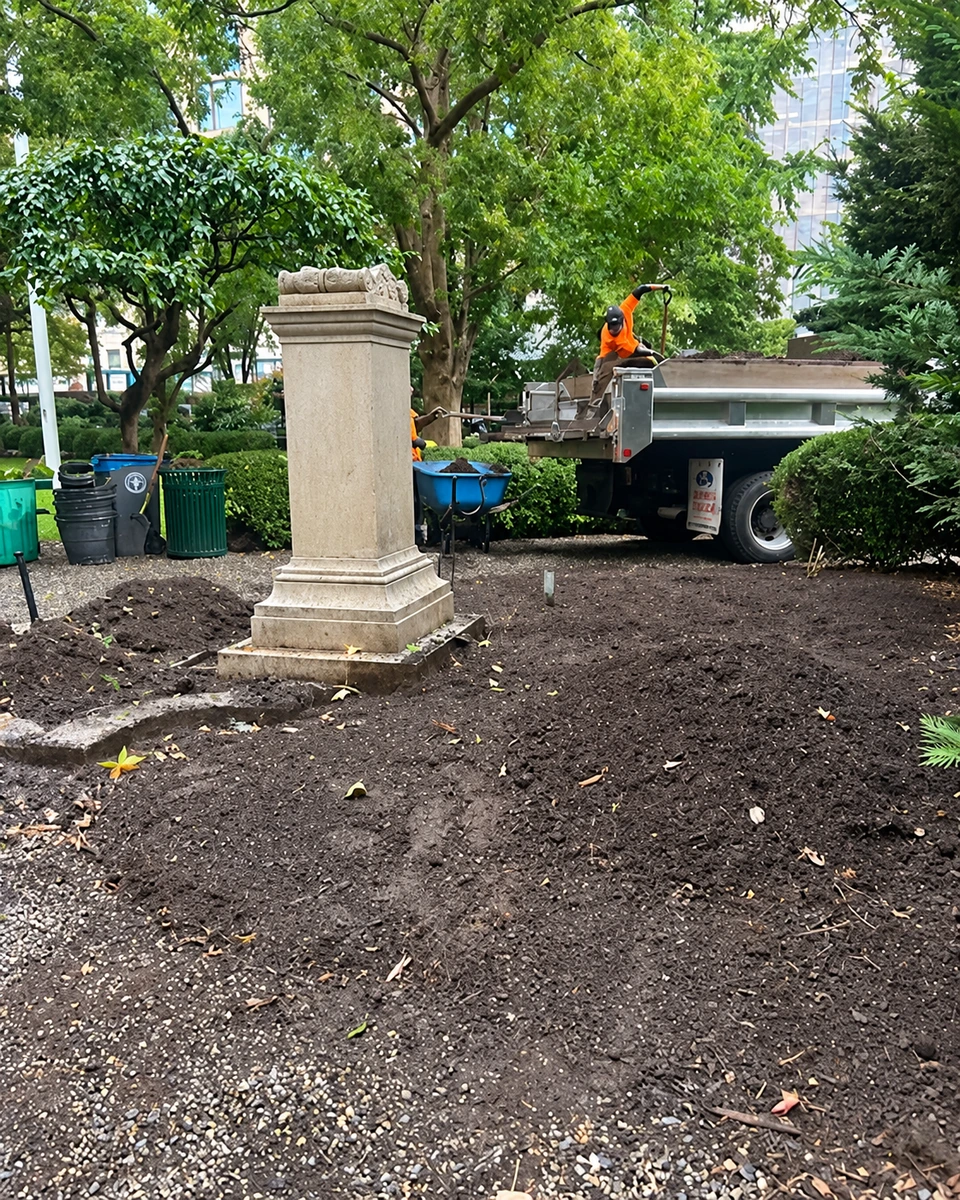 The marble memorial surrounded by bare earth after the basin stones have been removed.