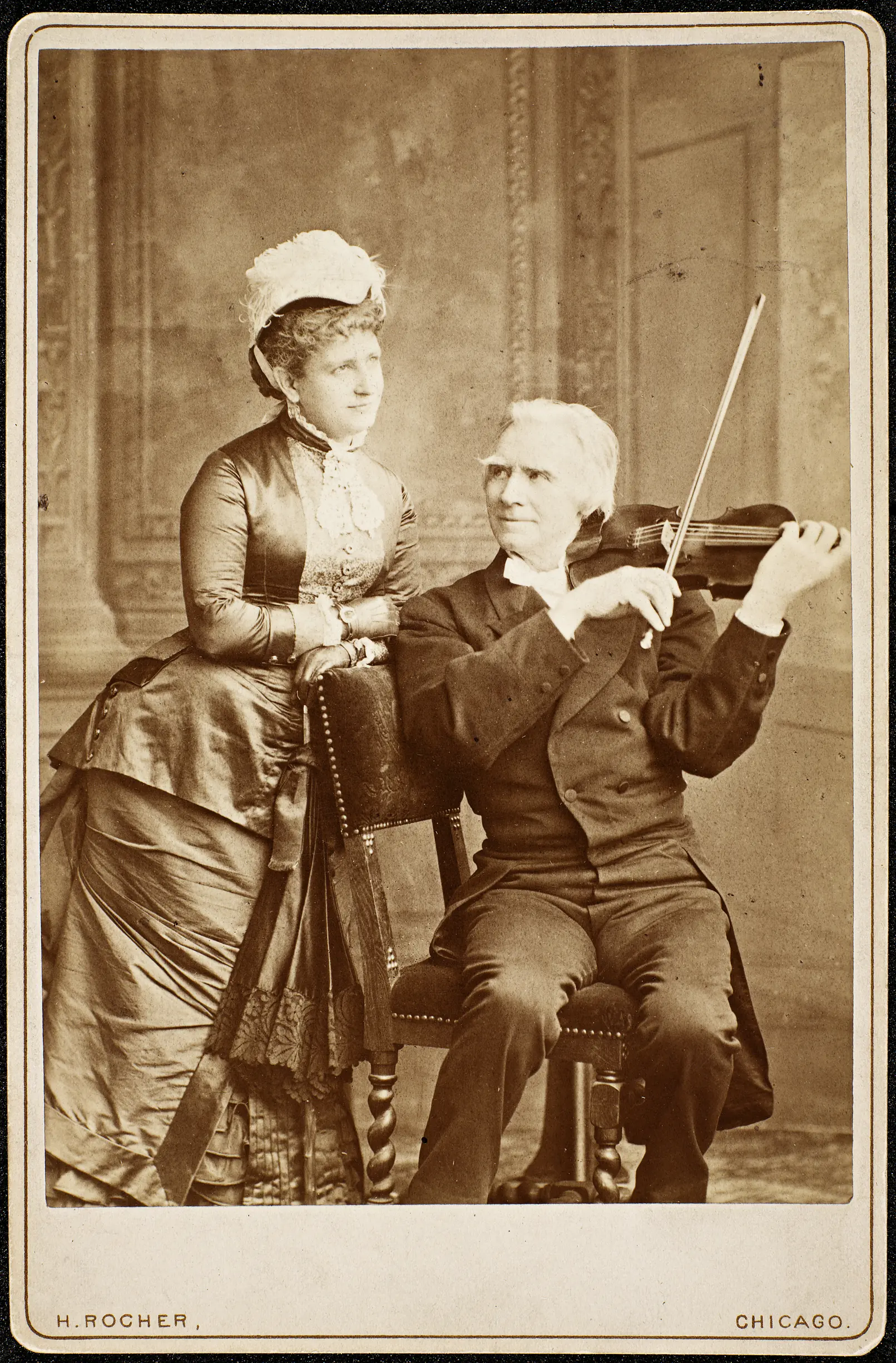 Emma Thursby standing beside seated Norwegian violinist Ole Bull, who holds his violin.