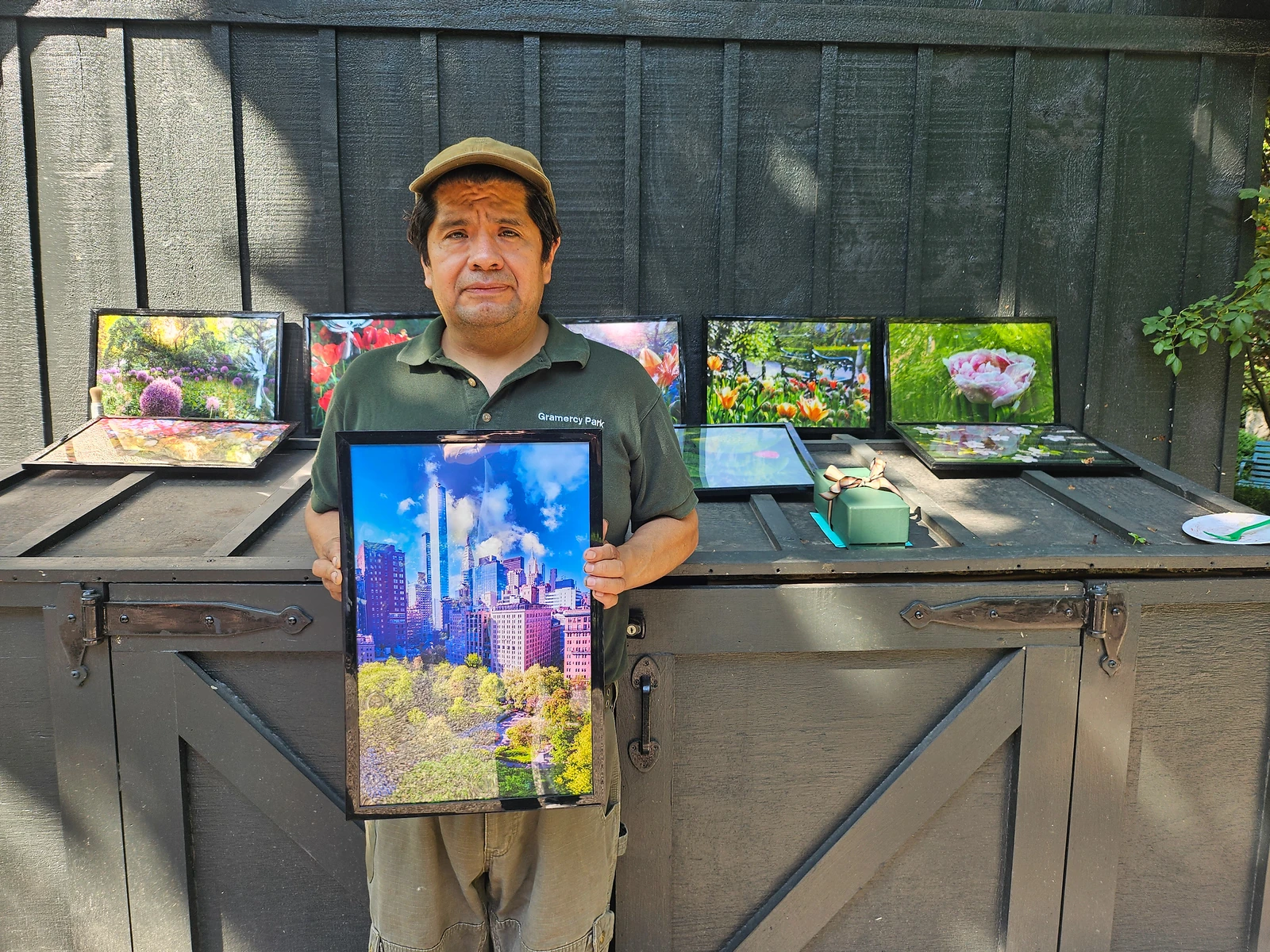 Amando holds a framed photograph of the Park beside a display of garden photographs.