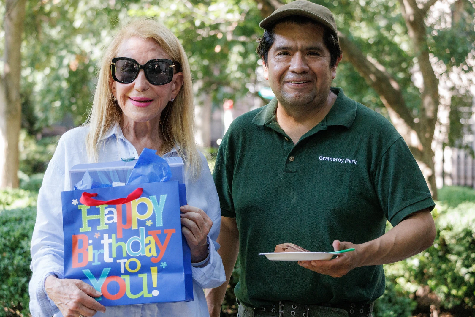 Amando and a neighbor stand together in the Park with a bright birthday gift bag.