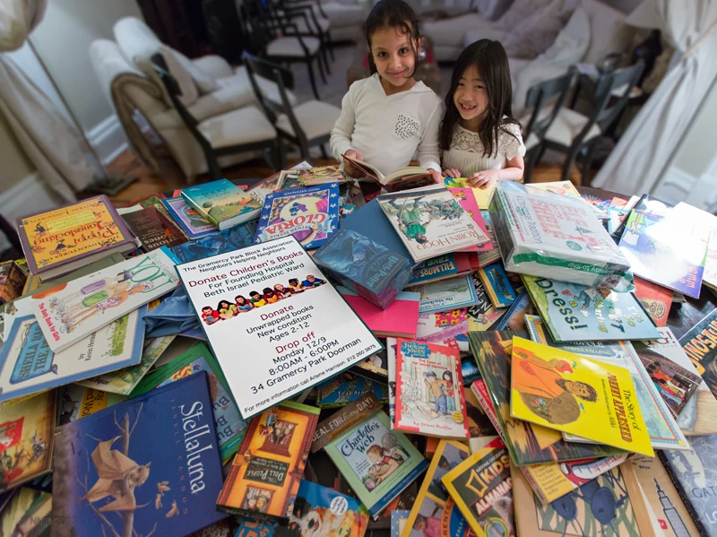 Two young volunteers sit behind a large collection of donated children’s books.