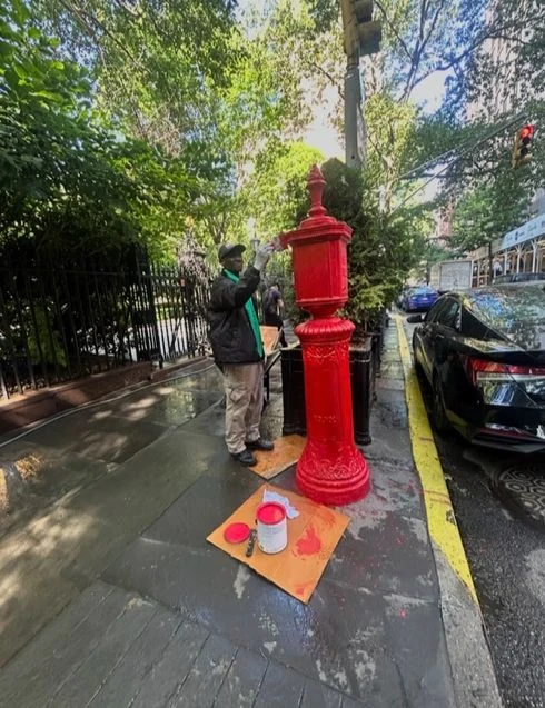A worker paints a red street fixture beside the Park fence.