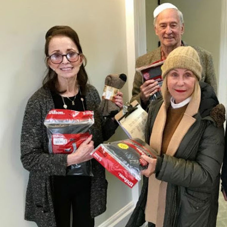 Three people display packages of clothing and other donated supplies.