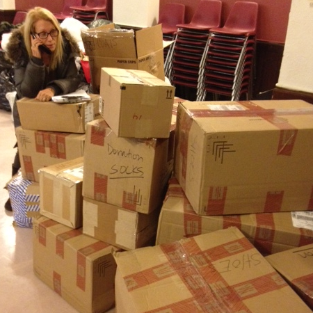 A woman stands behind a stack of taped cardboard donation boxes.