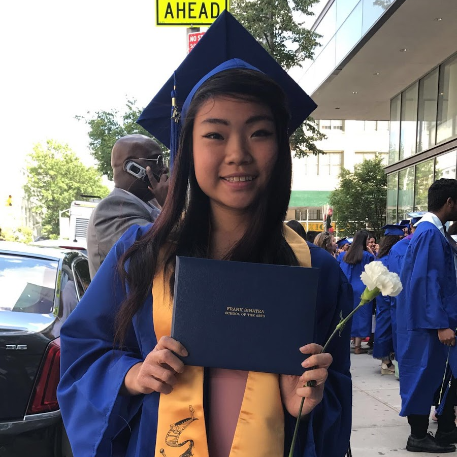 A graduate in a blue cap and gown holds a diploma cover outside.