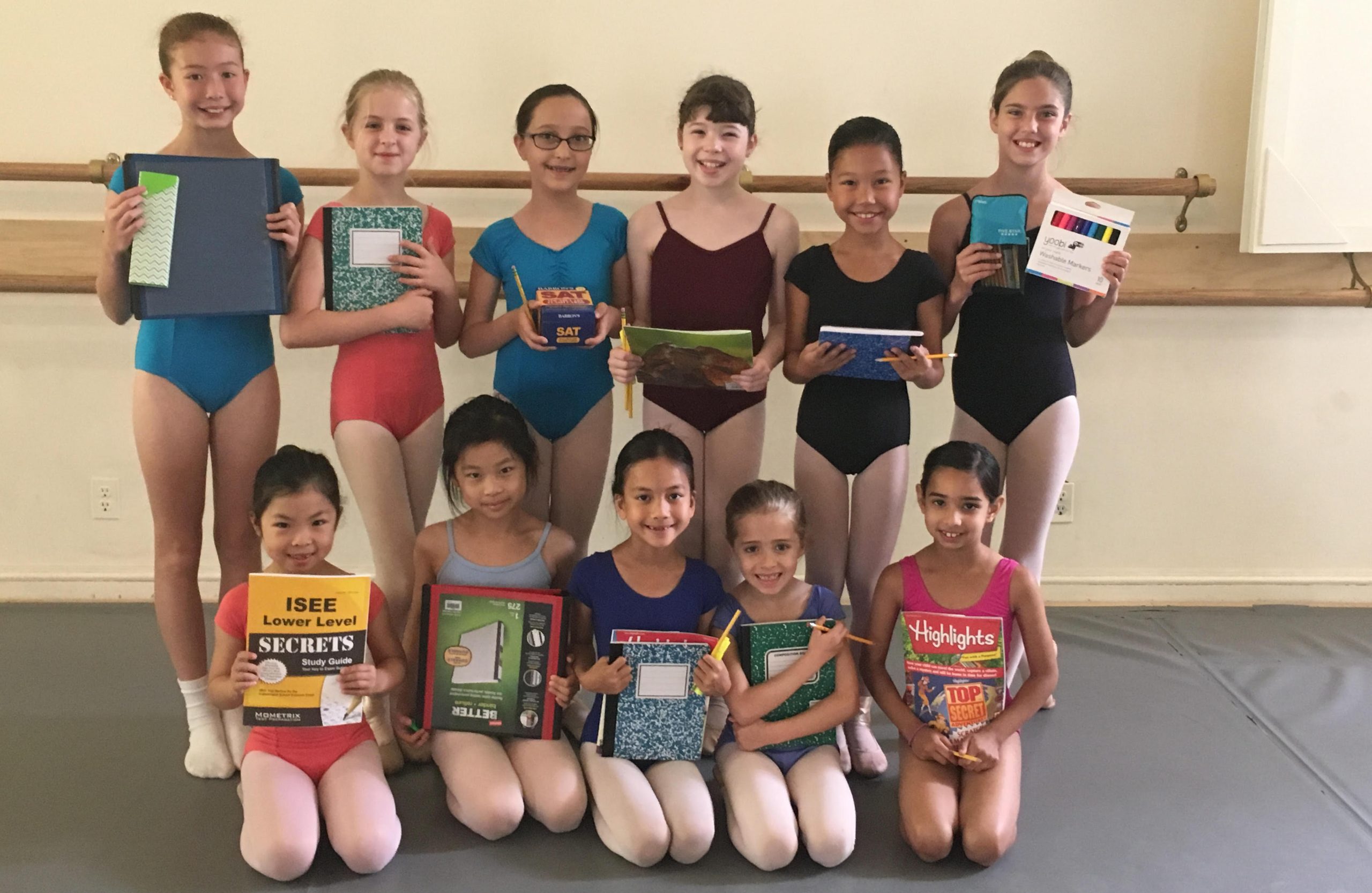 Children in dance clothes pose with books in a studio.