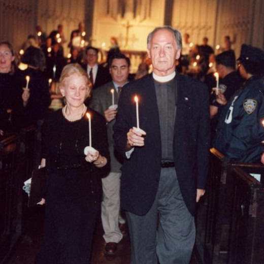 Two people hold lit candles in a church aisle with uniformed officers and other attendees behind them.