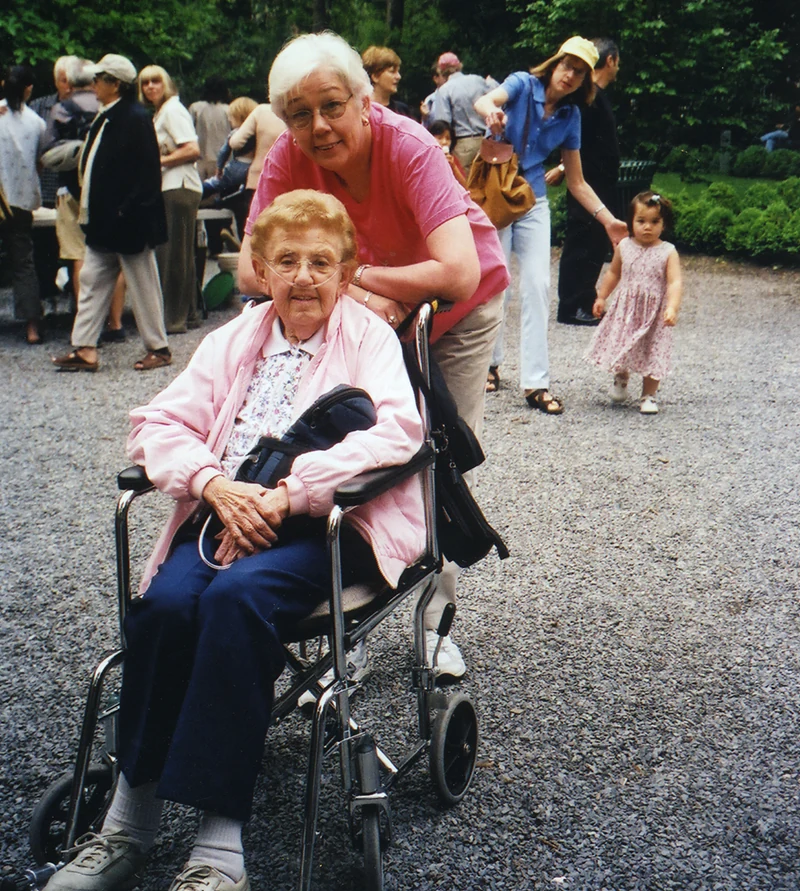 A woman stands behind a neighbor in a wheelchair in the Park.