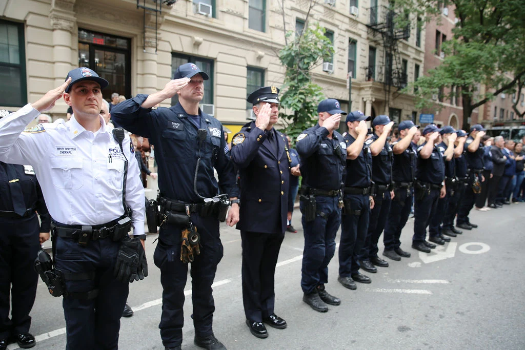 Uniformed officers salute in a line outside the 13th Precinct.