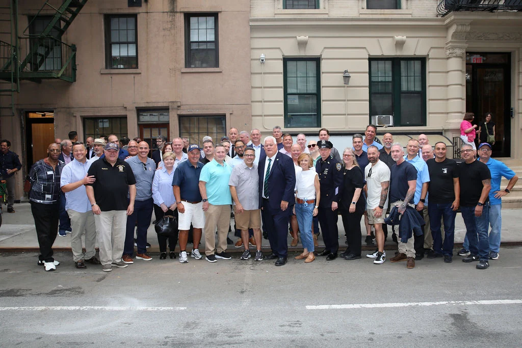 A group of attendees stands together on the sidewalk outside the precinct.