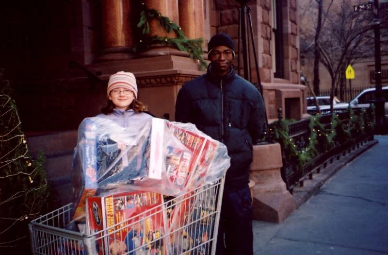 A young volunteer and a Kenmore Hall staff member stand beside a cart filled with toys.