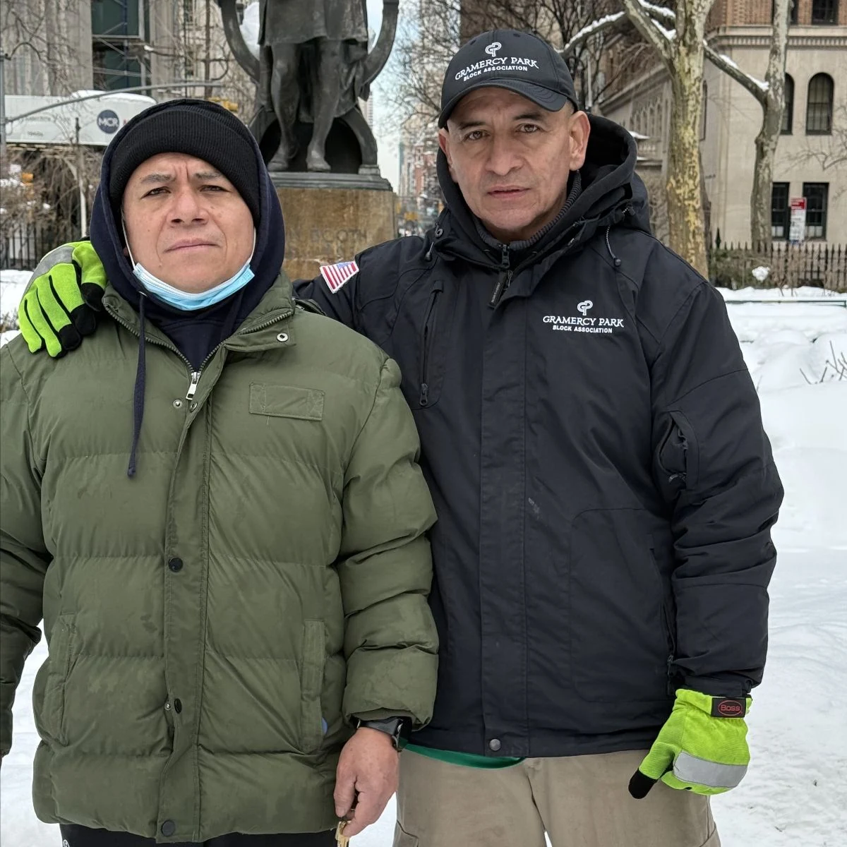 Two workers in winter jackets and gloves stand together after a snowstorm.